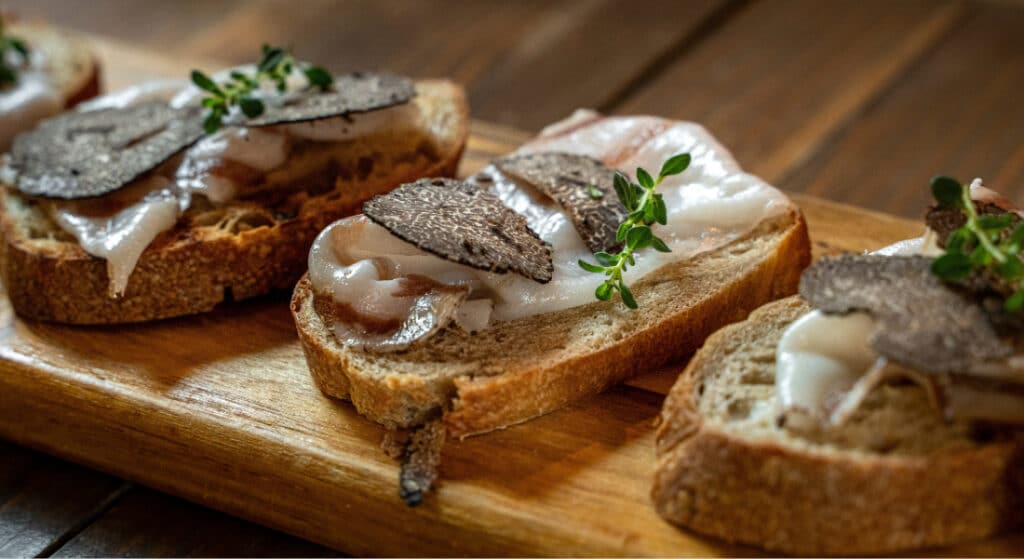 Bruschetta gastronomique garnie de lard artisanal, de fines lamelles de truffe noire et de thym frais sur du pain rustique.