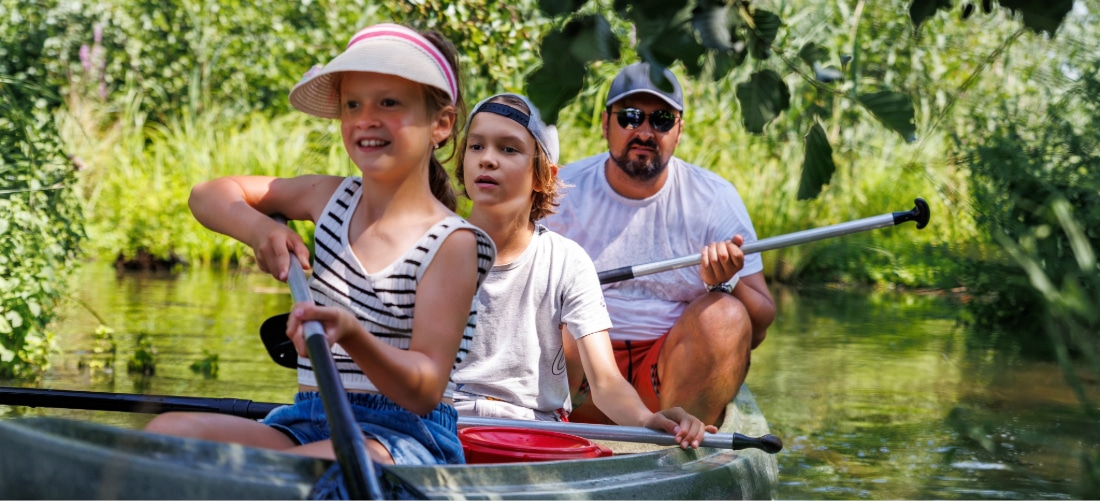 Un homme et deux enfants s'amusent à faire du canoë de location sur l'eau, par une chaude et belle journée d'été, tout en portant des gilets de sauvetage orange vif.